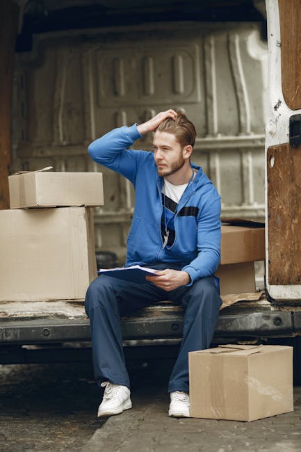A spacious room during a home relocation process showing neatly packed cardboard boxes of various sizes stacked on a wooden floor near a doorway. Some boxes are covered with brown packing paper, while